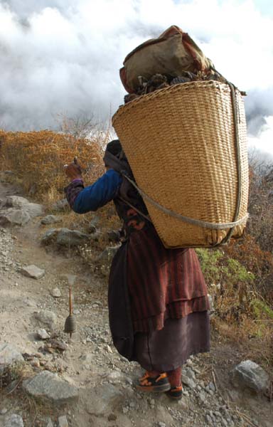 This woman is spinning wool as she walks up the hill with her heavy load